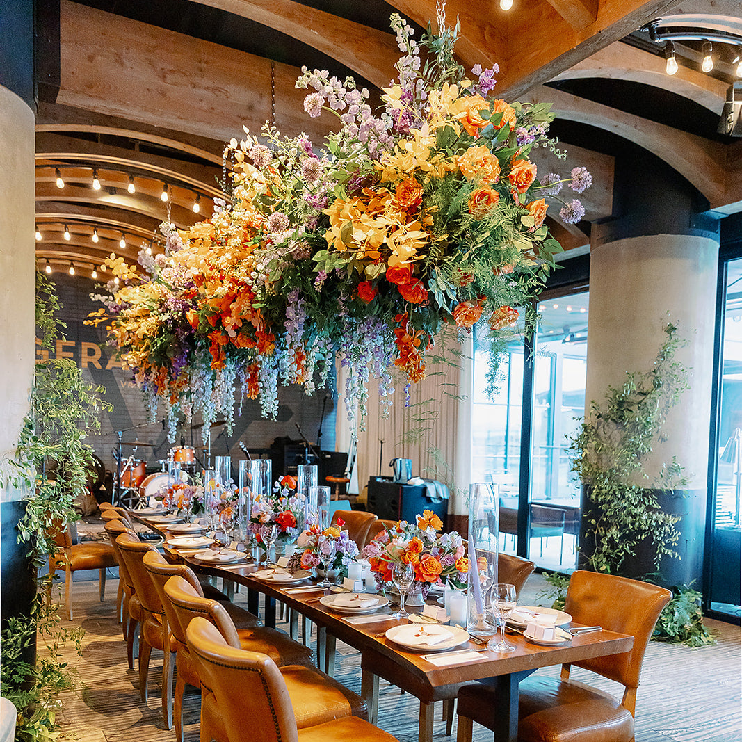 Hanging florals over a long table with floral centerpieces and candles in glass pillars for a private event by Posey Floral