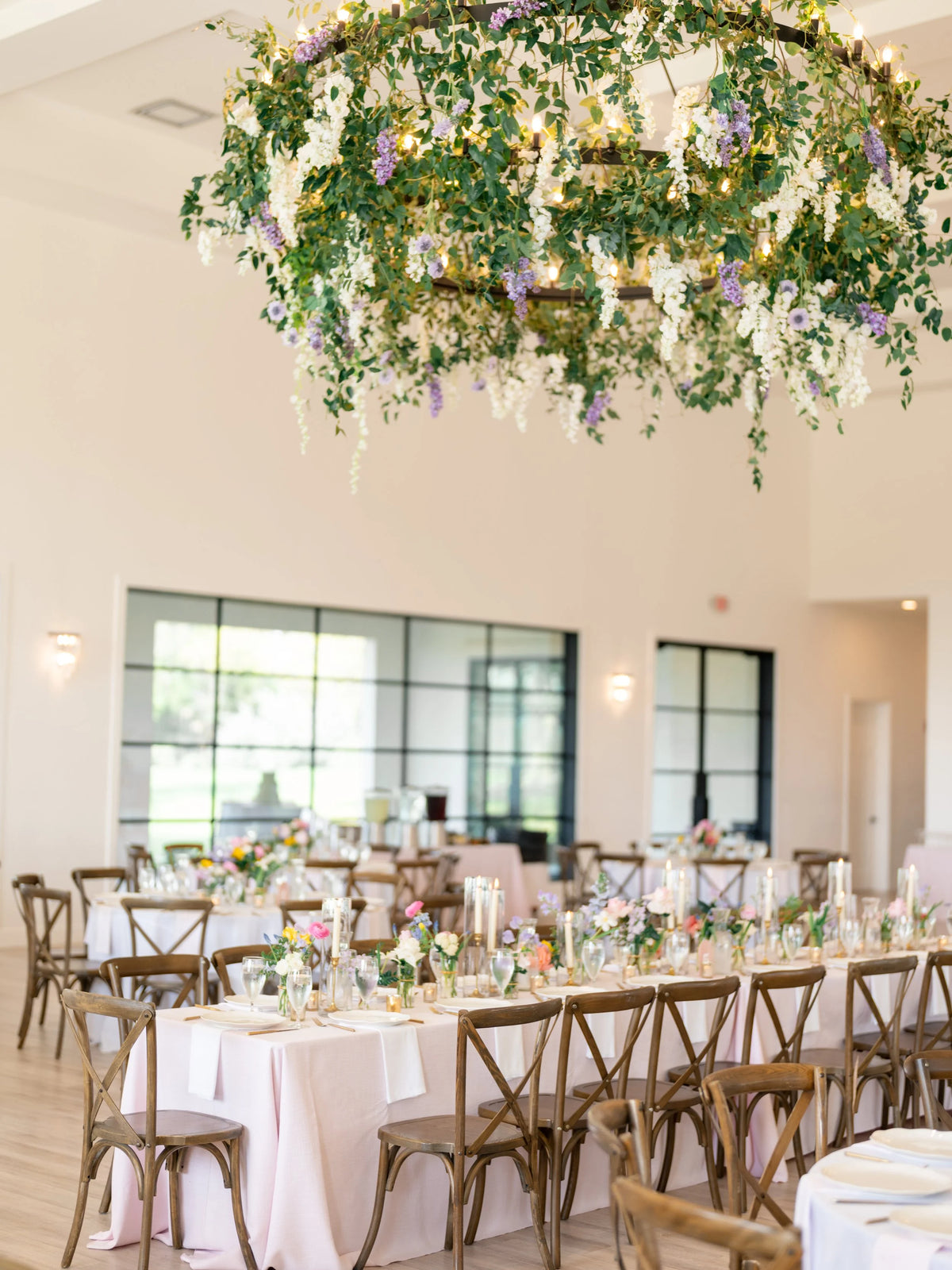 Wedding flowers at The Arlo in Austin. Hanging greenery and blue and white florals, with dining tables covered in bud vases, glass pillars, and taper candles. Floral design by Posey Floral. 
