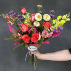 Bouquet of colorful flowers held by a person against a blue background for online floral delivery in Austin
