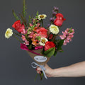 Bouquet of flowers held by a hand against a light purple background Austin texas delivery