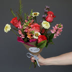 Bouquet of flowers held by a hand against a light purple background Austin texas delivery