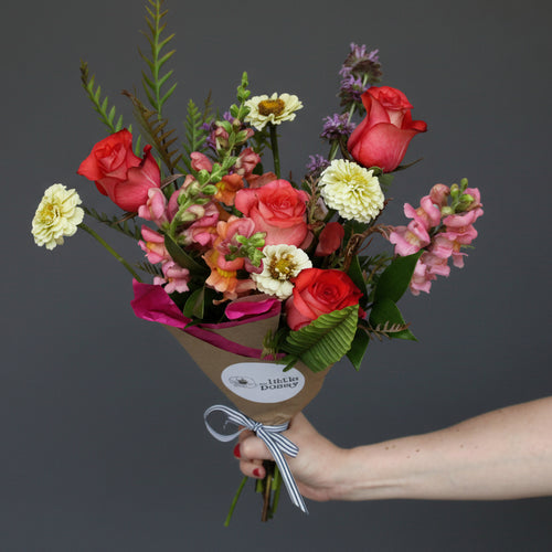 Bouquet of flowers held by a hand against a light purple background Austin texas delivery