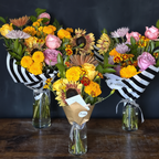 Three flower bouquets with striped paper and vases on a wooden surface against a dark background for online floral delivery in Austin