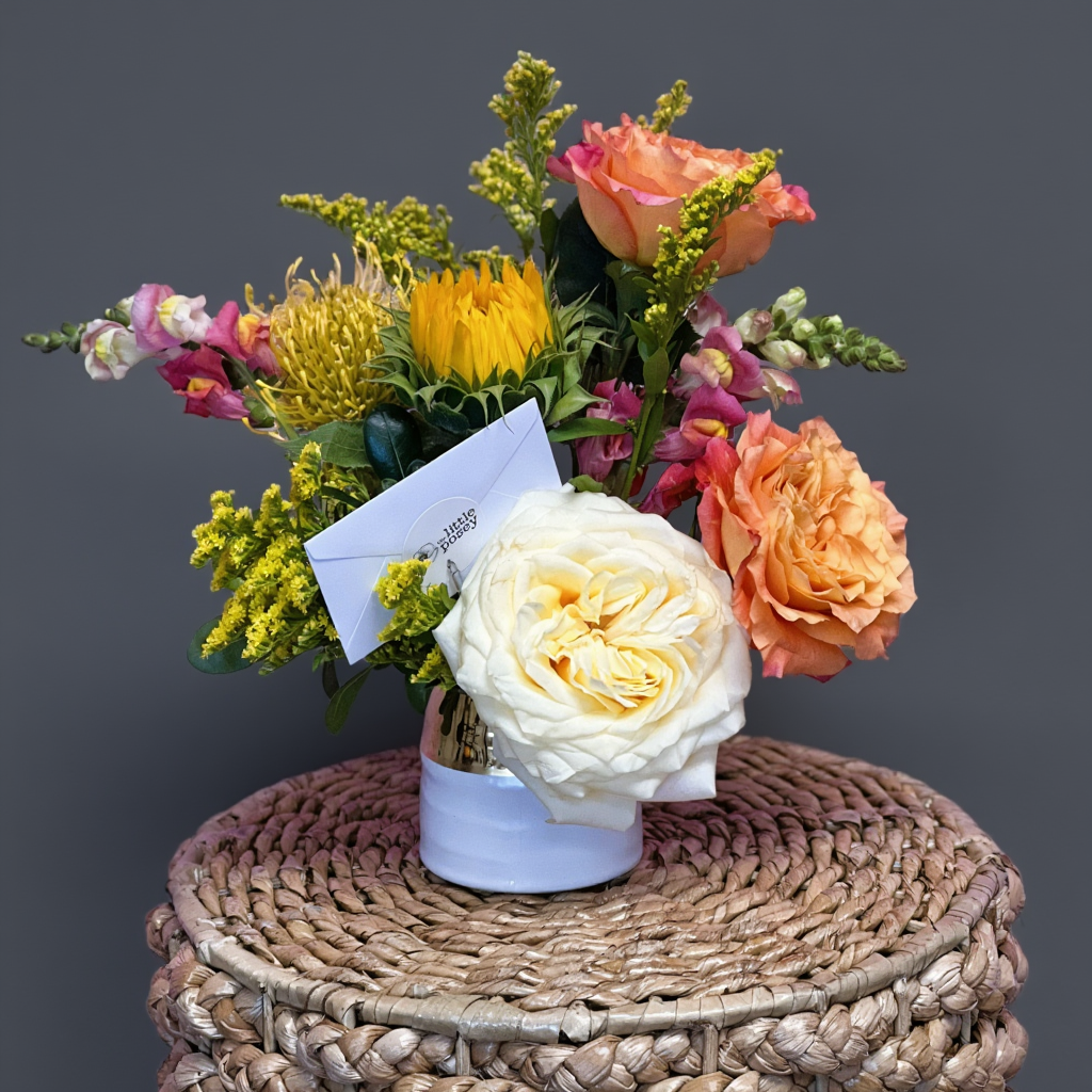 Bouquet of flowers with a card on a woven surface against a dark background delivery in Austin texas with luxe blooms