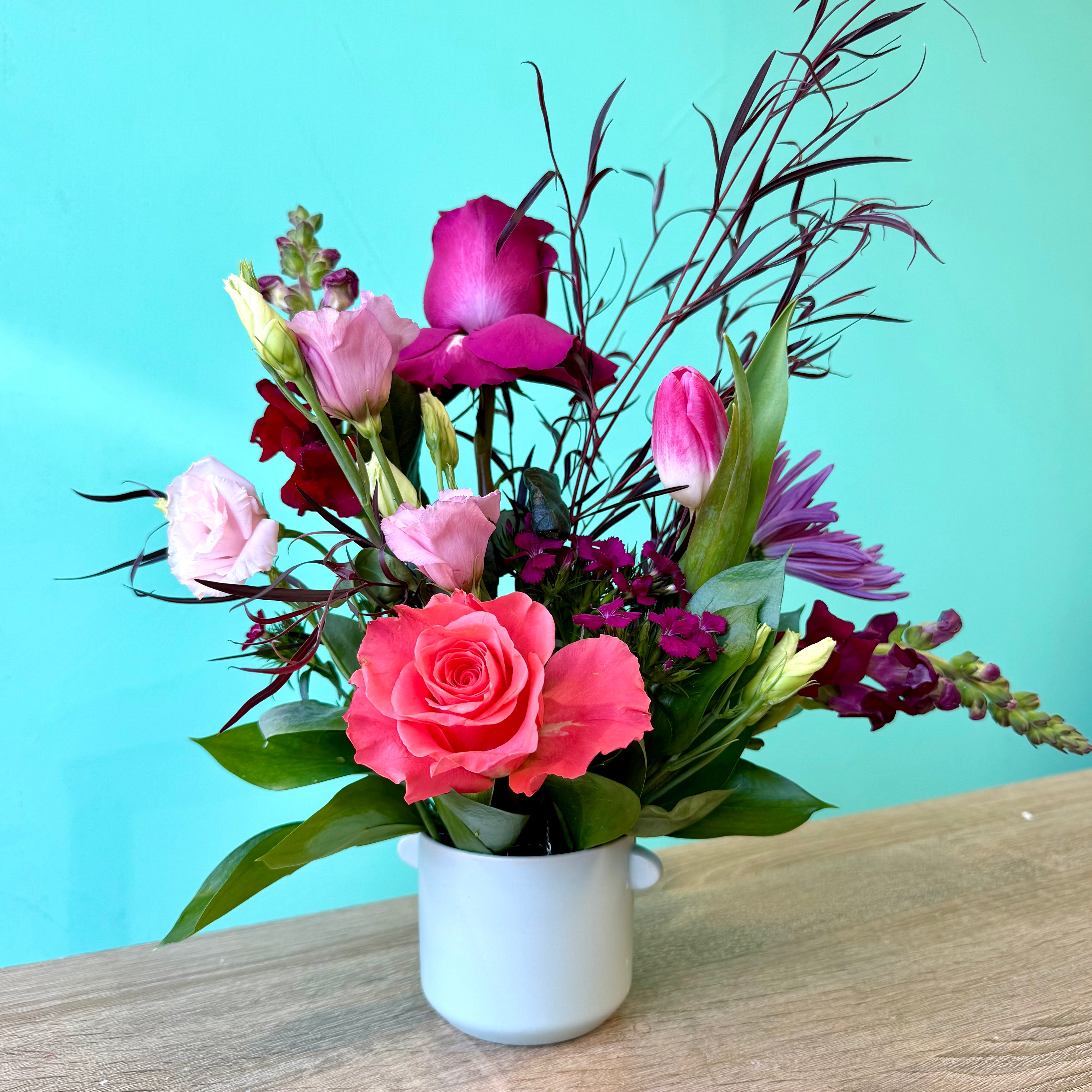 Designer arrangement of flowers in a white vase on a wooden surface with a teal background