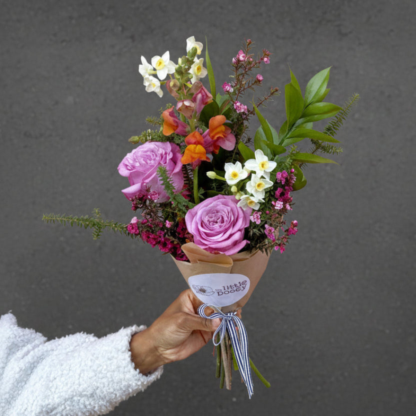 Bouquet of fresh flowers held by a person against a pink background