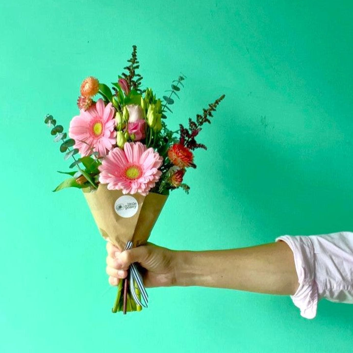 Hand holding a bouquet of flowers with colorful daisies against a teal background