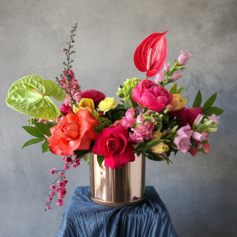 Colorful flower arrangement in a metallic vase against a turquoise background hand designed in Austin TX with delivery