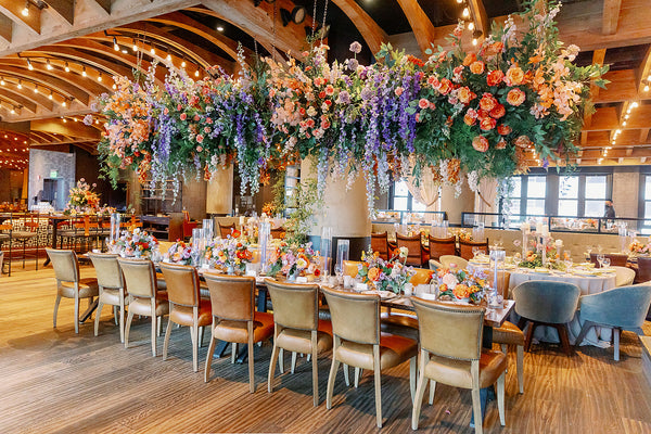 Special event florist Austin. Rehearsal dinners, buyouts. Decorative floral arrangements hanging above a long table set for a formal event in a large room with wooden beams.