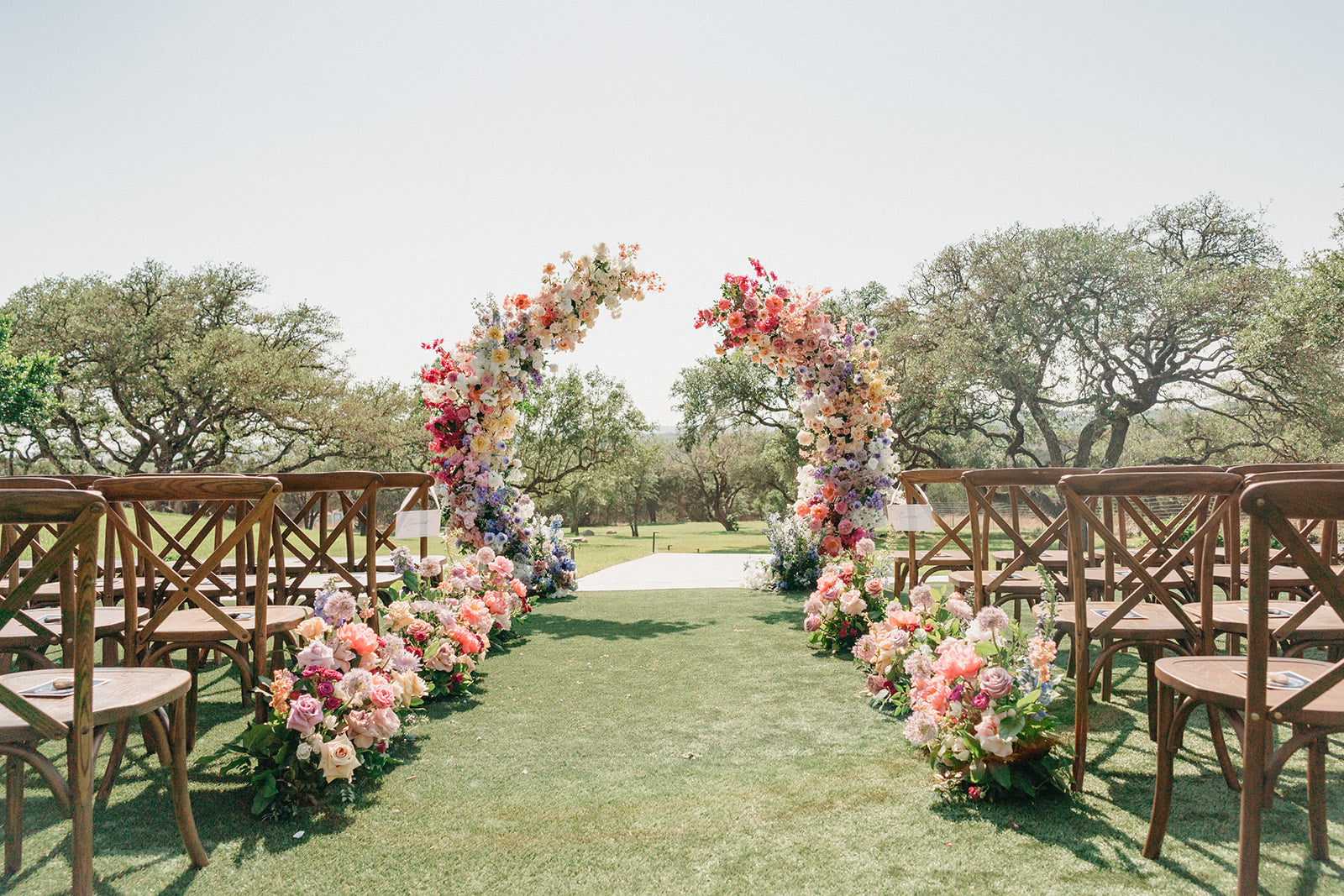 Floral archway setup for an outdoor wedding event with wooden chairs on a grassy area at Four Seasons Austin TX wedding