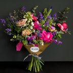 Affordable Bouquet of colorful flowers wrapped in brown paper with a visible brand label on a dark background. for online floral delivery in Austin