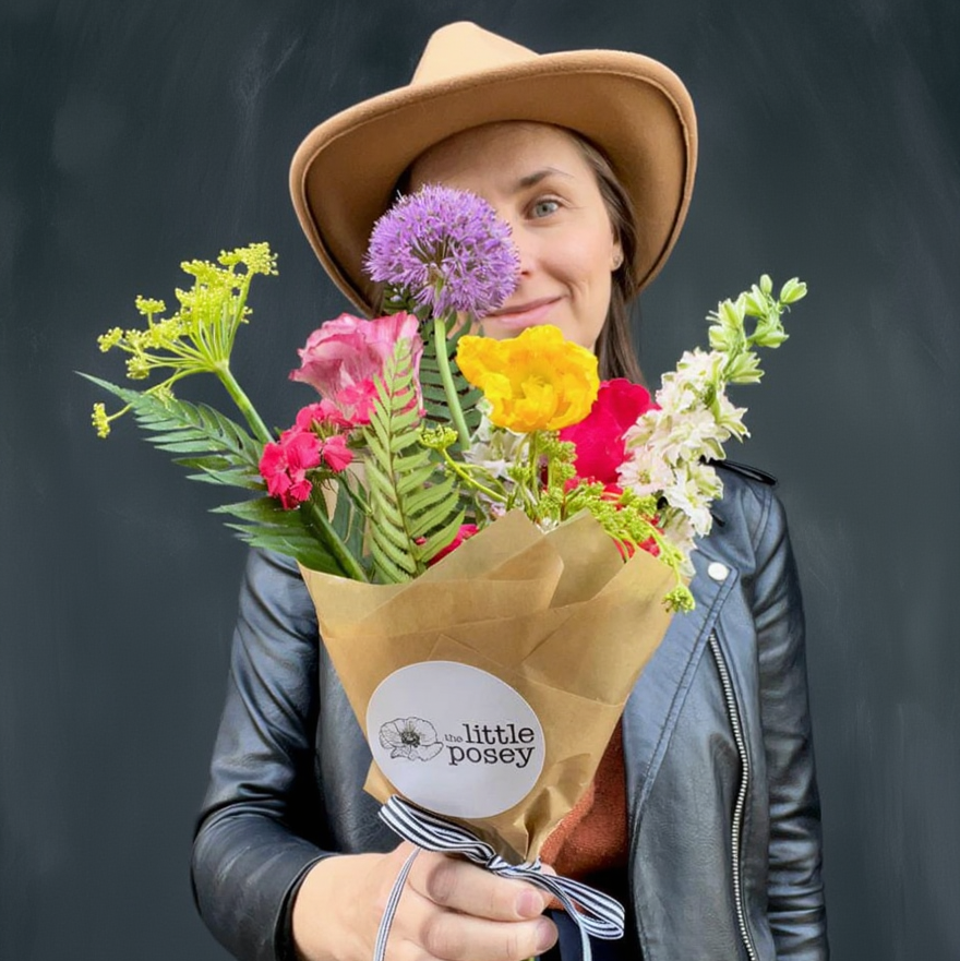 Person holding a bouquet of flowers with 'Little Posey' branding against a dark background